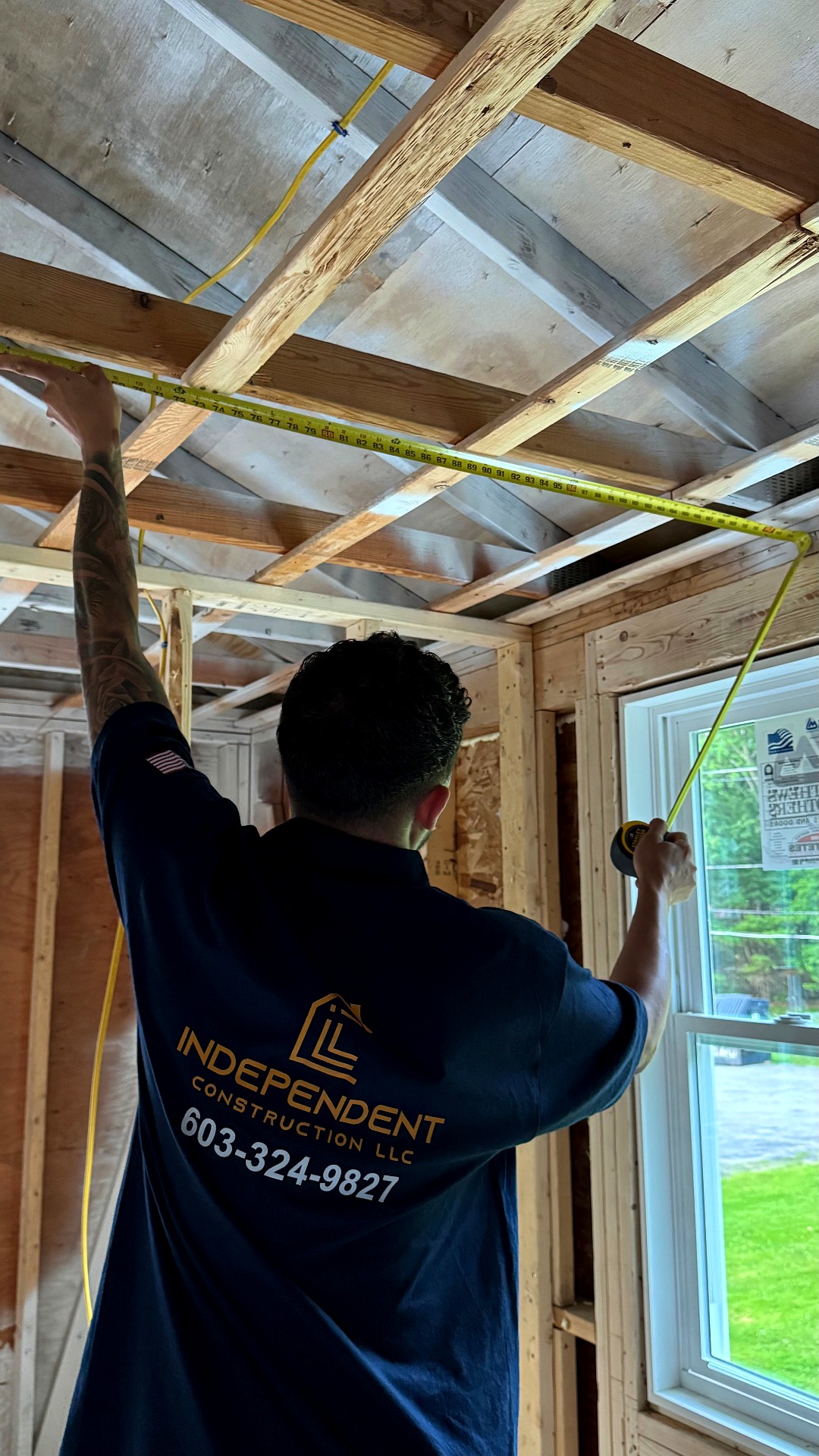 Independent Construction crew member measuring ceiling joists in a framed-out room